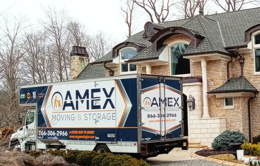 An AMEX Moving & Storage truck parked outside a large stone house